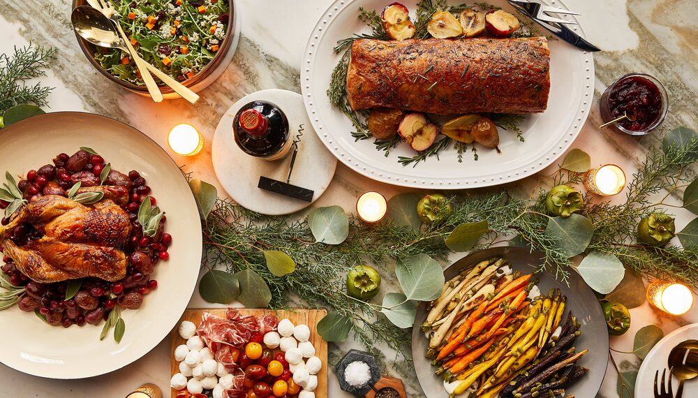 Holiday tablescape with roasted mains, sides, wine, and greenery.